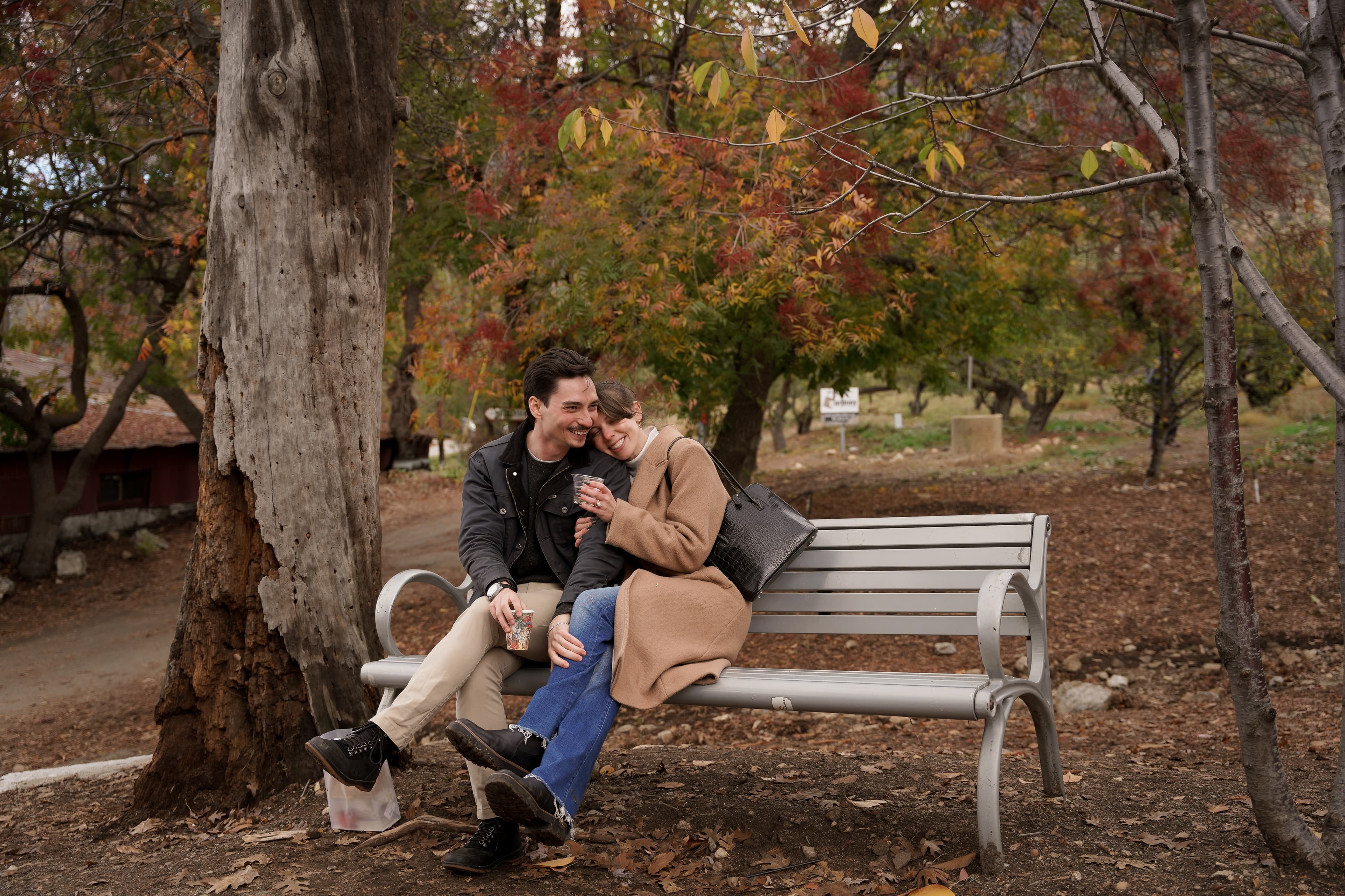 Jax and Jo sharing a happy moment on a bench beneath autumn trees