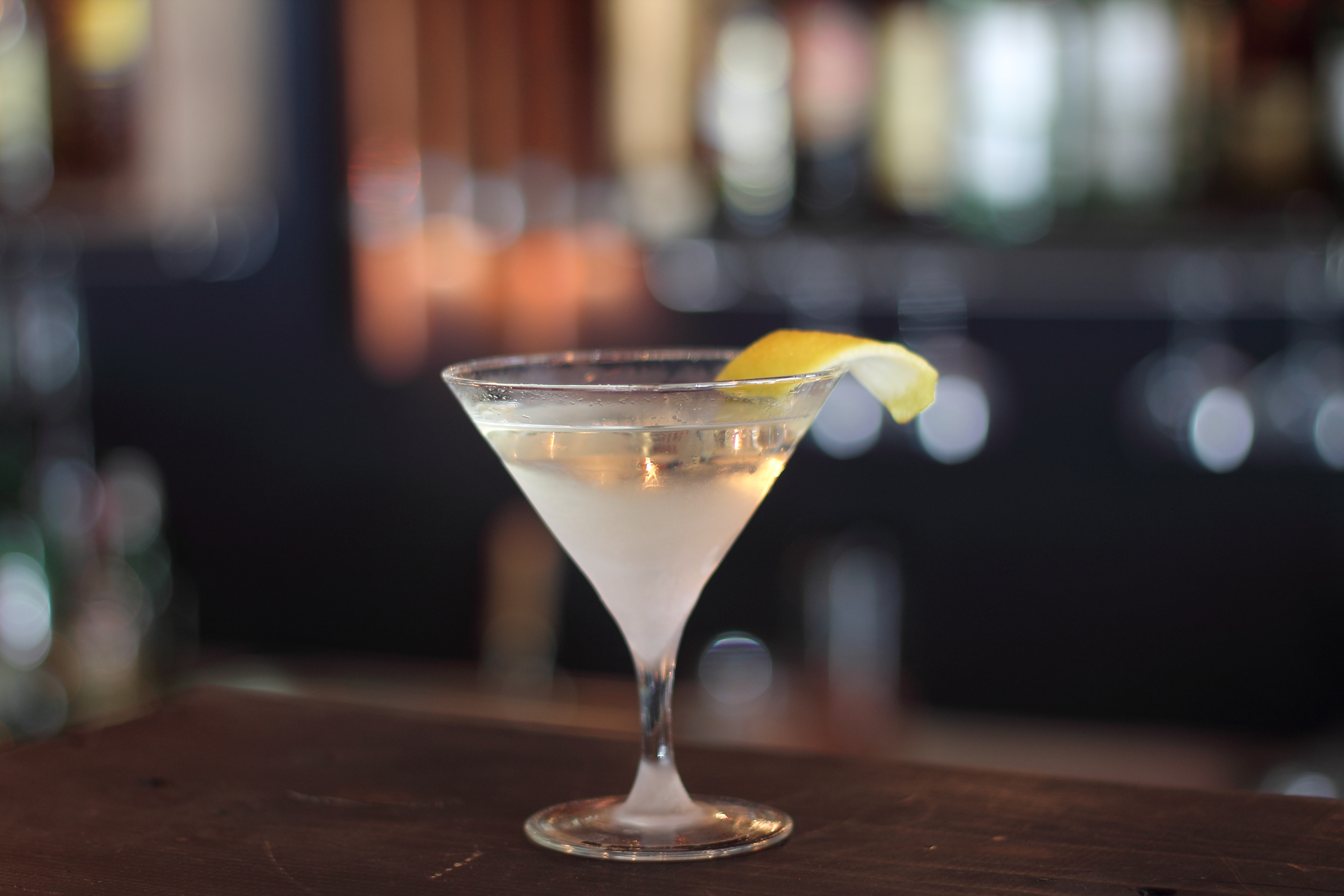 A martini with a lemon twist on a bar table