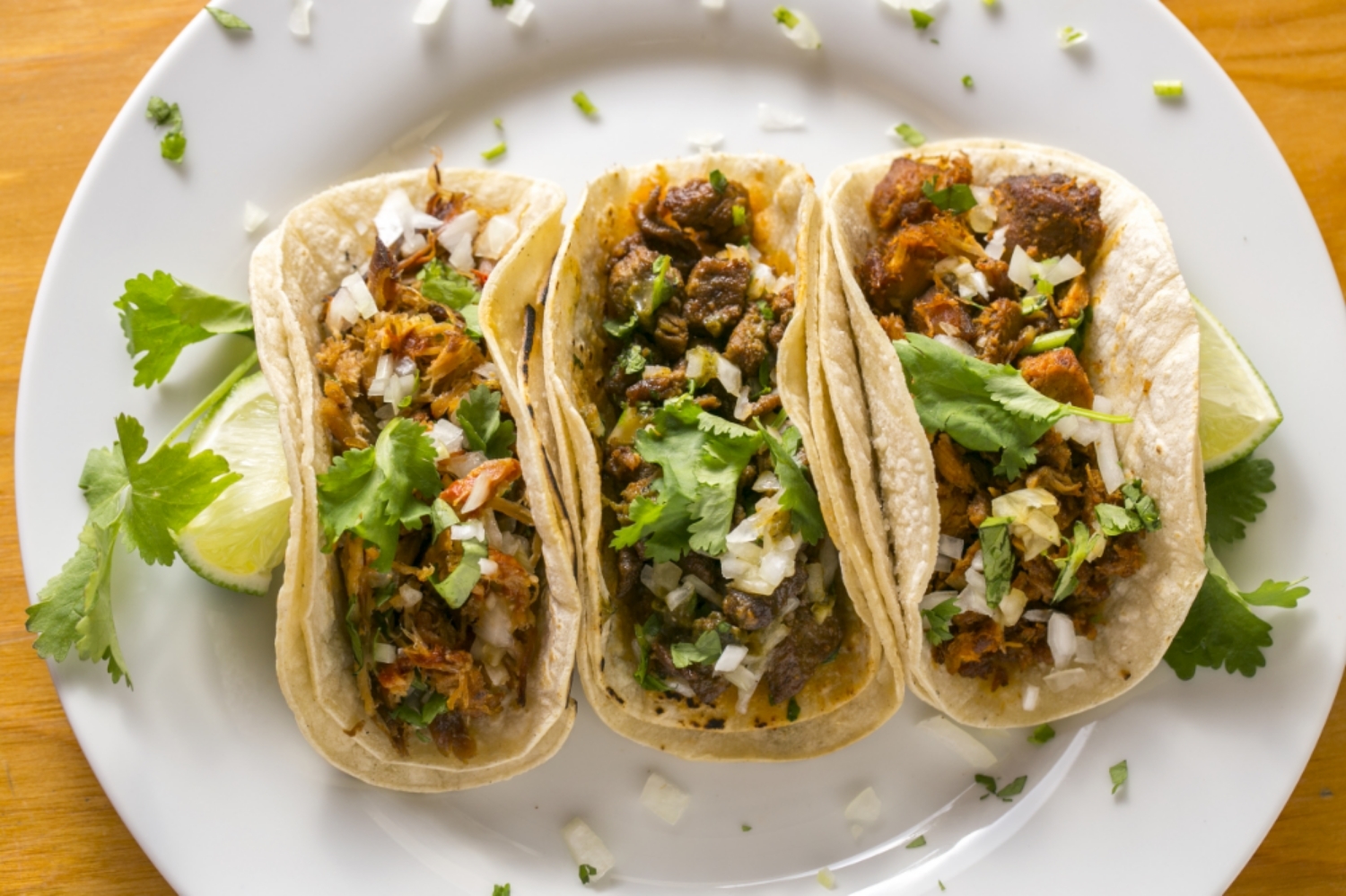 Three tacos with cilantro and lime on a plate